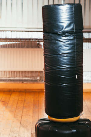 Punching bag for boxing at gym interior. Close up of boxing equipment at sport room. Black punching bag on wooden floor at gymの写真素材