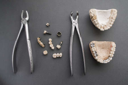 Tools for making prosthesis layout lay out. Professional materials for dental implantation training. Top view on bone forceps, gypsum jaws and dental implants and crowns on gray backgroundの写真素材