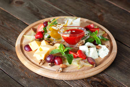 Fruits and cheese oh catering platter top view. Wooden board with variety of cheese and fruits with red and yellow sauces on dark wooden background. Wine snack setの写真素材