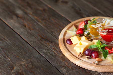 Cheese with grapes and sauces on wood copyspace. Catering platter with gouda cheese, grapes and red and yellow sauces, decorated with mint and nutsの写真素材