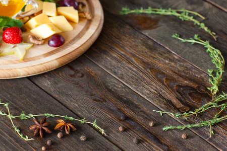 Frame on wood from cheese plate and herbs copy space. Top view on dark wooden background with wine snack catering platter and herbs, making frame with void.の写真素材