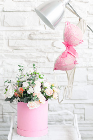 Female lingerie on lamp above vase with flowers. Nightstand in woman boudoir with flowers and table lamp with turned pink bra on it.の写真素材