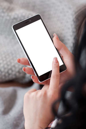 Brunette holding mobile phone with white screen. Smartphone with copyspace on screen in female hands. Woman touching empty screen of cell phoneの写真素材