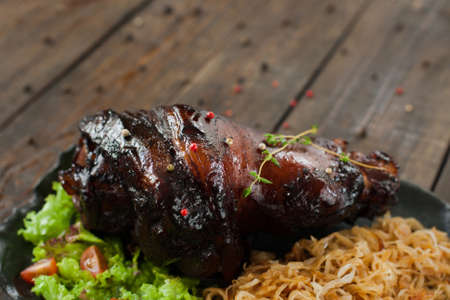 Baked pork leg with braised cabbage copyspace. Black plate with backed pork leg with braised cabbage, lettuce and tomatoes on wooden background. Free space and Junk foodの写真素材