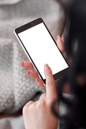 Brunette using cell phone with white screen. White screen for advertisement of smartphone in female hands. Woman fingering smartphoneの写真素材