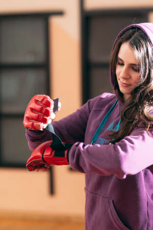 Smiling female athlete put on boxing gloves at gym. Pretty girl in purple sporsuit put on red boxing gloves before active workout. Women self defence conceptの写真素材