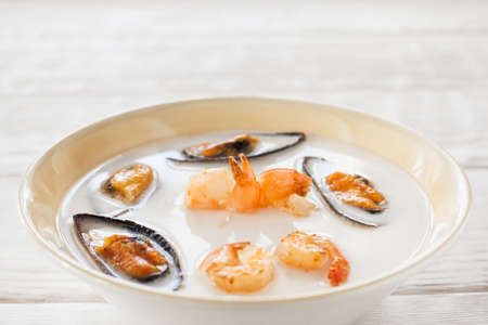 Cream-soup with shrimps and mussels copyspace. Bowl with seafood cream-soup on white wooden background. White soup with mussels and shrimps in bowlの写真素材