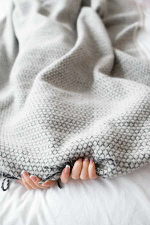 Woman hiding from the problems under the gray blanket. Photo of bed with gray blanket and two female hands, free space for text. Fear, introvert, loneliness backgroundの写真素材