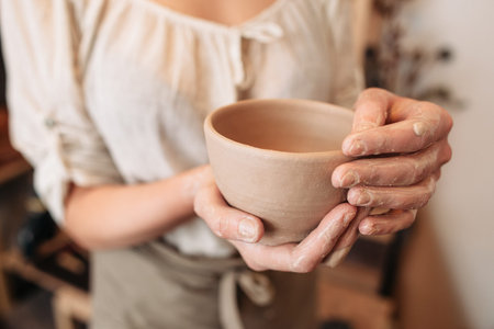 Potter woman keeping clay bowl in dirty palms closeup. Unrecognizable female craftsman with her creation at studioの写真素材