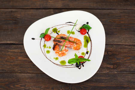 Dish of tasty grilled shrimps flat lay, copyspace. Top view on white triangle plate with fried prawns, decorated by chef at restaurant, on dark wooden background, flat layの写真素材