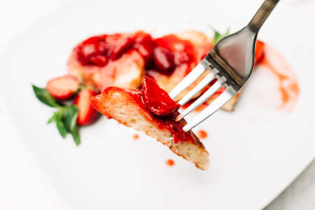 Fork with strawberry pancake on blurred meal background. Eating dessert at restaurant with special cutlery. Appetizing sweet flapjack with berry jam diningの写真素材