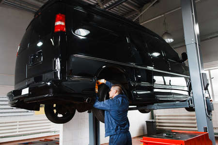 Black minibus on repair in garage. Mechanic working with SUV, lifted on elevator at modern auto service stationの写真素材