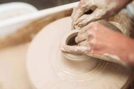 Pottery classes, student making clay pot on wheel. Close-up of dirty hands, sculpting clay crockeryの写真素材