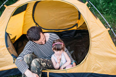 Dad with his little daughter in tent on camping. Interesting family journey, travel photoの写真素材