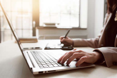Web designer working on project, photo processing. Close-up of female hands, working on laptop and graphic tablet in modern officeの写真素材