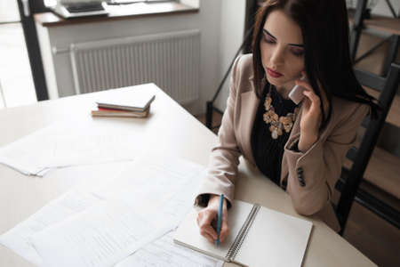Beautiful office girl in formal wear speaking on mobile phone and receiving orders, taking business call. Responsible secretary, good worker, successの写真素材