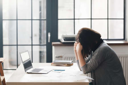 Female entrepreneur sitting in office and looks confused with laptop on desk.の写真素材