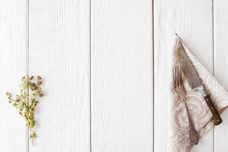 White wooden background with old cutlery, flat lay. Free space on wood with knife and fork on napkin and herb, frameの写真素材