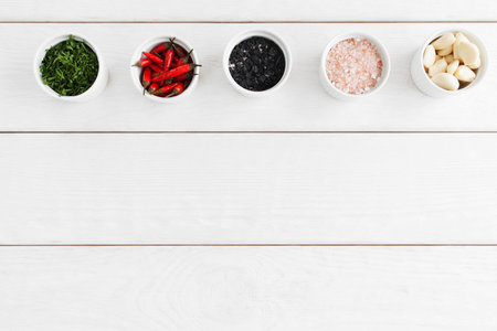 Bowls with black and pink sea salt, parsley, chili and garlic, free space.