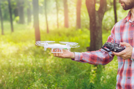 Unrecognizable man running quadrocopter in forest.