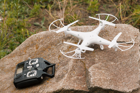White quadrocopter on stone with remote control, close-up.