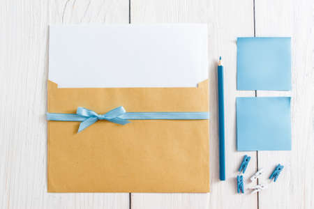 Top view on kit of envelope with blank paper and blue ribbon, pencil, pins and sticker on white background.の写真素材