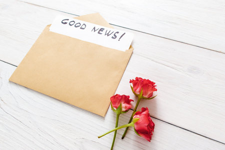 Good news note in brown envelope with red flowers on white wooden backgroundの写真素材