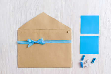Brown envelope with blue ribbon and stickers on white wooden background, flat lay. Greeting card handmade set, blank paper. It's a boy note conceptの写真素材