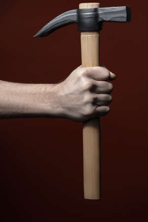 Strong man's hand holding hammer on dark red background. Handyman with household equipment. Handicraft, diy repair and fixing conceptの写真素材