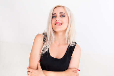 Confident beautiful woman in black dress biting her lip. Young attractive blonde with folded arms looking at camera with arrogant expression, white backgroundの写真素材