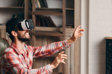 Happy bearded man using vr glasses. Young guy in virtual reality headset playing game. Modern technology, innovation, cyberspace, entertainment conceptの写真素材