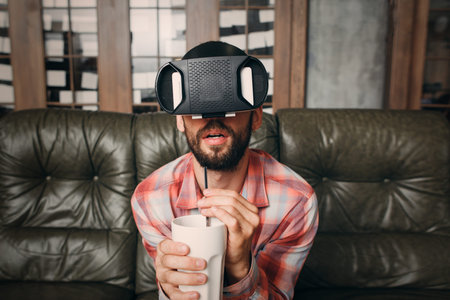 Man watching exciting movie in vr goggles. Bearded guy in virtual reality headset forgot about...