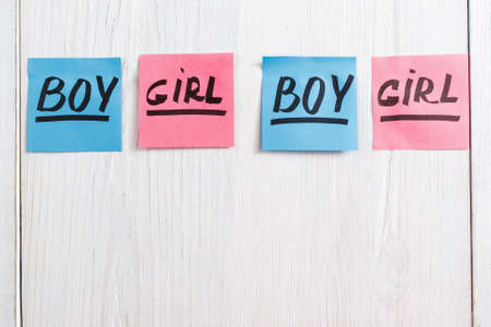 Colorful stickers with boy and girl text, copy space. Composition of pink and blue papers on white wooden background. It's a girl and boy twins conceptの写真素材
