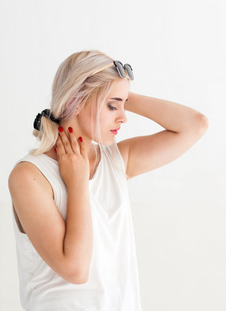Beautiful sensitive woman touching her neck. Side view of young attractive blonde in sunglasses, white backgroundの写真素材