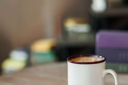 Cup of cappuccino on blurred office background. Fresh tasty beverage in ceramic mug, coffee break concept, free spaceの写真素材