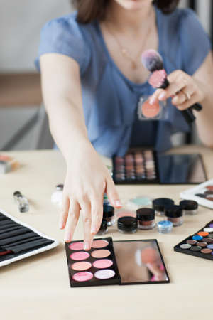 Artist taking rouge with brush, visagiste workplace. Close-up of stylist hand on palette with pink shades bluster. Beauty, makeup, cosmetics conceptの写真素材