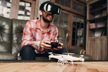 Man try to control drone in vr glasses. White unmanned aerial vehicle with camera on table before...
