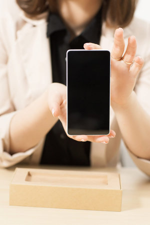 Unrecognizable woman shows new model of smartphone with blank screen. Modern technology presentation. Recent phone sample in female handsの写真素材