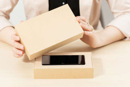 Woman opening box with new smartphone, close-up. Female customer lifting lid from package with her order. Delivery service. online shopping, parcel opening , gift conceptの写真素材