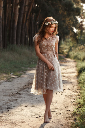 Young woman in wreath walking in forest barefoot. Beautiful girl in polka-dot dress relaxing in nature, she steps on path with pine cones, free space.の写真素材