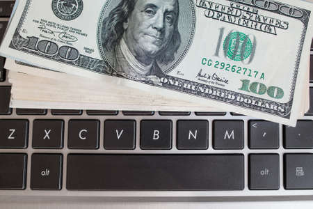 Batch of one hundred dollar bills on keyboard, close-up. American money banknote on laptop. Income through internet, programming conceptの写真素材