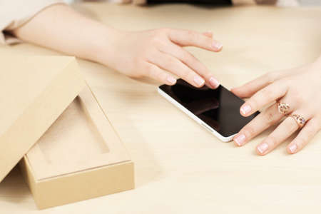 Woman using new smartphone near carton box. Female hands testing touch screen of resent gadget. Modern technology presentation, online shopping conceptの写真素材