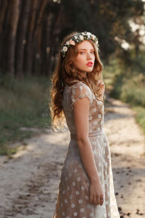 Beautiful girl walking in forest on sunset. Young woman in polka-dot gray dress strolling in nature, path between pine trees background, free spaceの写真素材