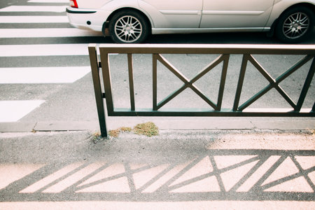 Steel fence near pedestrian zebra, going car on background. Close-up of metal barricade separating...