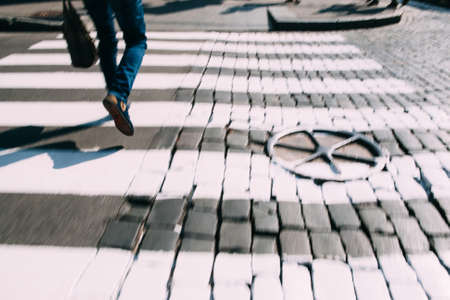 Pedestrian zebra on asphalt and paving stone. Close-up of crossroad with running legs, busy people, european city, blurry photoの写真素材