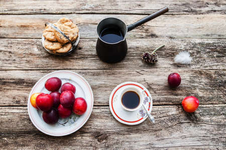 Inspirational early morning breakfast in country, flat lay. Top view on old rustic wooden table with fresh coffee in cup and pot, tasty plums and cookies.の写真素材