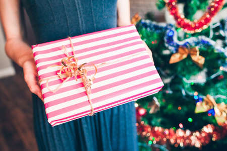 Woman holding present box near Christmas tree. Xmas gift unpacking. Happy family, joy, love conceptの写真素材