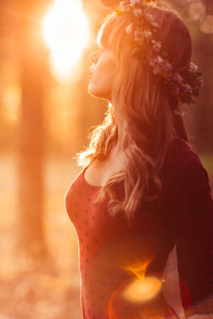 Profile of beautiful woman in wreath, sunset flare, free space. Attractive blonde relaxing in forest. Fashion, beauty, art conceptの写真素材