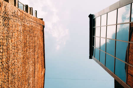 Modern glass and brick buildings, view from below. Blue sky in frame of two houses. Present and old architecture conceptの写真素材