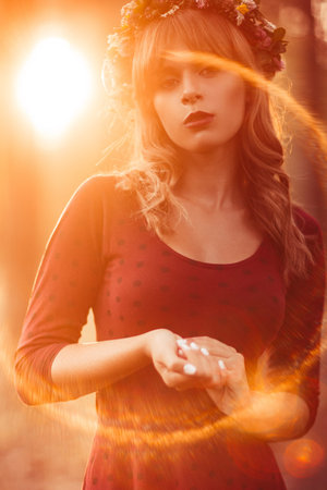 Beautiful woman in wreath, lens flare effect. Attractive blonde looking at camera relaxing in forest. Fashion, beauty, art conceptの写真素材